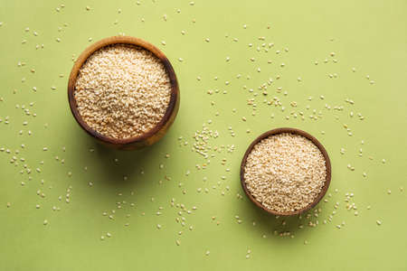 Wooden bowls with sesame seeds on green background