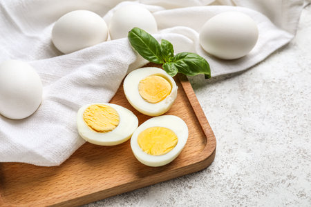 Wooden board with halves of boiled chicken eggs on light background, closeup