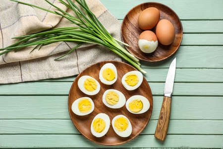 Composition with plates of boiled chicken eggs, green onion and knife on color wooden background