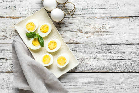 Plate with halves of boiled chicken eggs on light wooden background