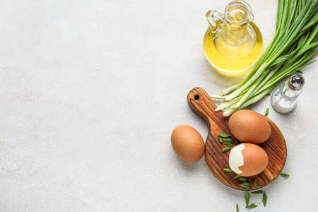 Composition with chicken eggs, salt, oil and green onion on light background