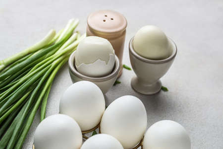 Holders with chicken eggs and green onion on light background, closeup