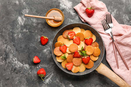 Composition with frying pan of mini pancakes, strawberry and honey on grunge backgroundの写真素材