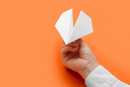 Woman with white paper plane on orange backgroundの写真素材