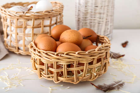 Wicker baskets with chicken eggs on white wooden tableの写真素材