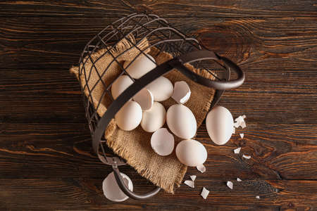 Overturned basket with chicken eggs and shell on wooden background