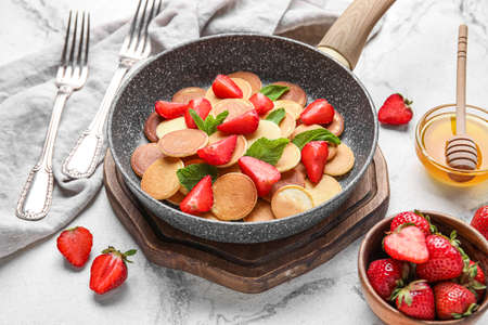 Wooden board with frying pan of mini pancakes and strawberry on light backgroundの写真素材