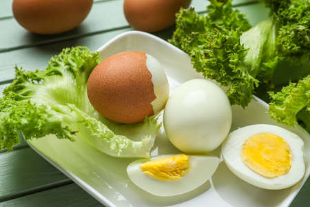 Plate with boiled chicken eggs and lettuce on table, closeup