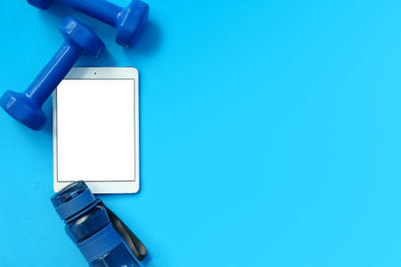 Modern tablet computer, dumbbells and bottle of water on blue background