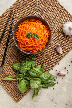 Composition with bowl of tasty korean carrot salad, spices and basil on light backgroundの写真素材