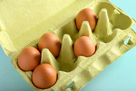 Cardboard holder with brown chicken eggs on color background