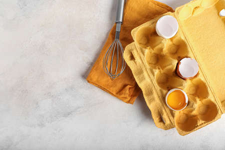 Holder with broken egg, shells and whisk on light background