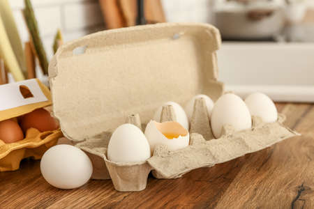 Cardboard holder with chicken eggs on table in kitchen