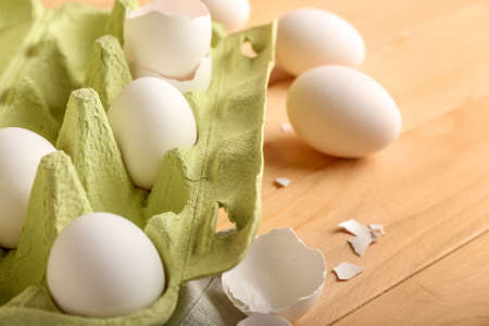 Cardboard holder with chicken eggs and shells on wooden background, closeup