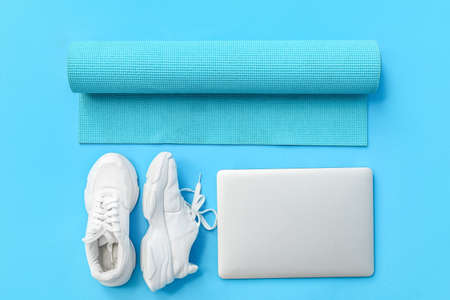 Modern laptop, sports shoes and yoga mat on color background
