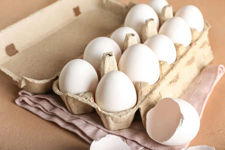 Cardboard holder with chicken eggs on color background, closeup
