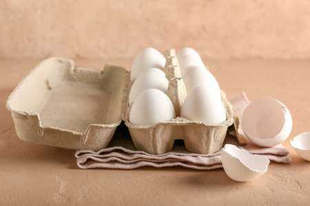 Cardboard holder with chicken eggs on color background