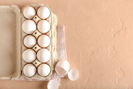Cardboard holder with chicken eggs on color background