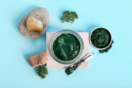 Composition with jar of spirulina facial mask, stones and powder on blue background