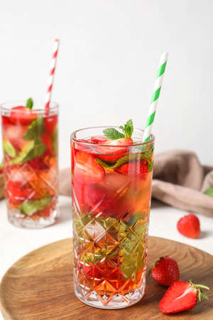 Wooden board with glass of strawberry lemonade on white background