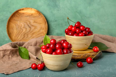 Bowls of sweet cherry on color background