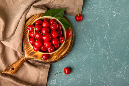Wooden board with bowl of sweet cherry on color backgroundの写真素材