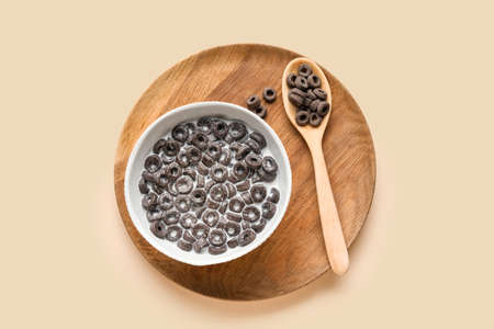 Bowl and spoon with tasty cereal rings and milk on color background