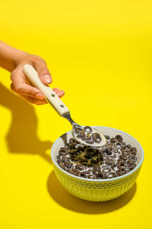 Female hand with spoon of cereal rings and milk on yellow background