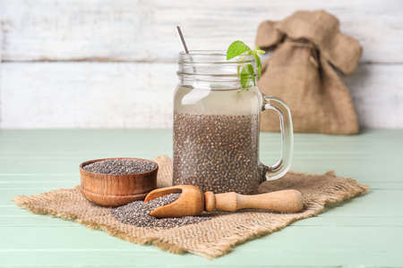 Glass jar of water with chia seeds, scoop and bowl on color wooden backgroundの写真素材