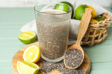 Glass of water with chia seeds, citrus fruits, spoon and board on green wooden tableの写真素材