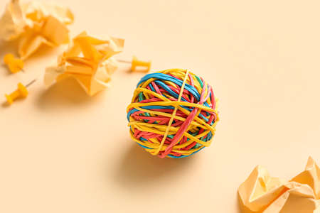 Colorful rubber band ball, crumpled paper and pins on beige background