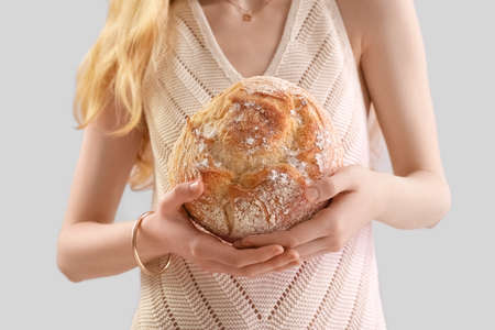 Young woman with fresh bread on gray background, closeup