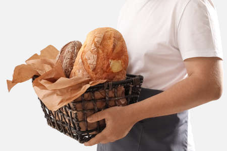 Man holding basket with loaves of fresh bread and parchment paper on light backgroundの写真素材