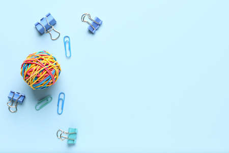 Colorful rubber band ball with paper clips on blue background