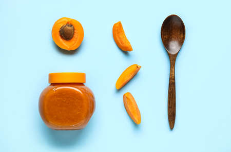 Composition with jar of tasty apricot jam, fruits and spoon on color backgroundの写真素材