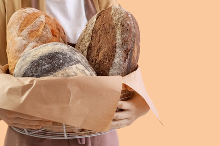 Young woman holding basket with fresh bread on beige background, closeupの写真素材