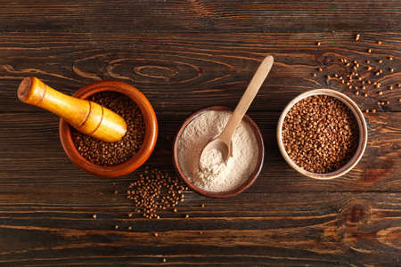 Bowls with flour, buckwheat grains and spoon on dark wooden backgroundの写真素材