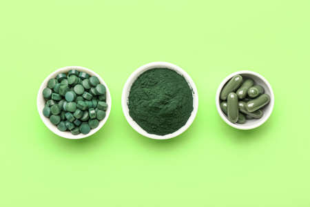 Bowls with spirulina pills and powder on green backgroundの写真素材