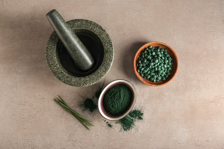 Bowls of spirulina powder, pills, mortar and pestle on beige backgroundの写真素材