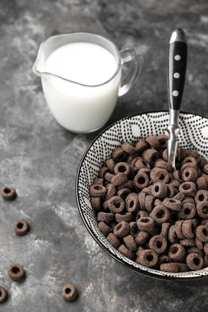 Bowl with black cereal rings and jug of milk on dark background, closeupの写真素材