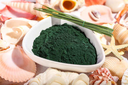 Bowl of spirulina powder and leaves on seashells