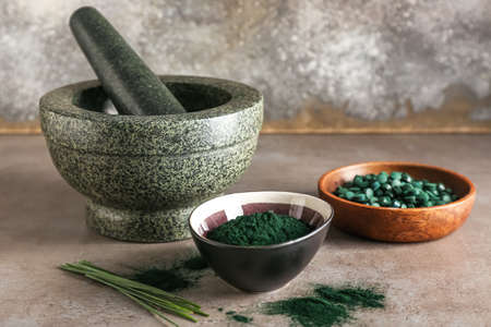 Bowls of spirulina powder, pills, mortar and pestle on grunge backgroundの写真素材