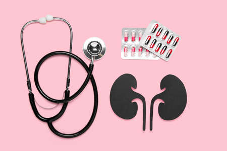 Paper kidneys with pills and stethoscope on pink background