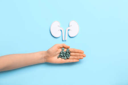 Woman with pills and paper kidneys on blue background