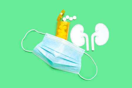Paper kidneys with bottle of pills and medical mask on green background