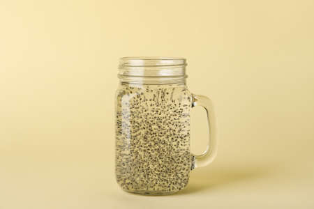 Mason jar of water with chia seeds on color background