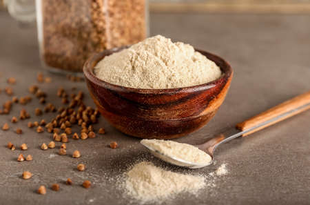 Bowl of flour and spoon with buckwheat grains on grunge backgroundの写真素材