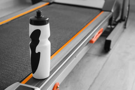 Bottle of water on modern treadmill in gym, closeup