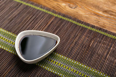 Bowl of soy sauce and bamboo mat on wooden background, closeupの写真素材
