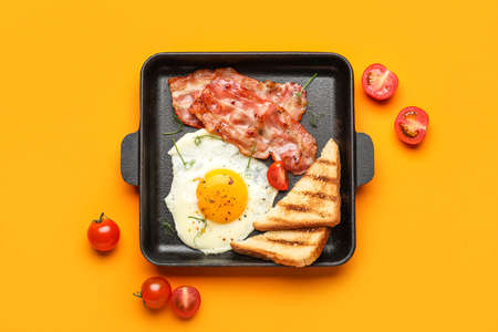 Frying pan with tasty fried egg, bacon, toasts and tomatoes on color backgroundの写真素材